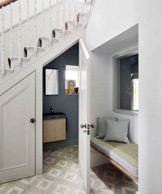 A cloakroom under the stairs with dark gray painted walls, a small sink and a mirror on the wall