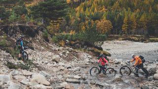 Three bikepackers pushing their bikes across a river in Scotland