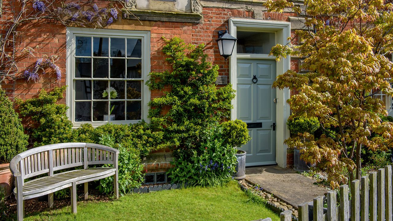 A front garden with grass, a bench and wisteria climbing the house exterior