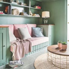 Green painted room with built-in shelves on the wall, and a built-in sofa with pink cushions on it