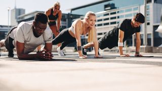 Group of three people performing a plank on a rooftop with a person behind them standing hands on knees