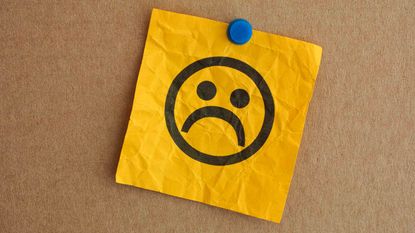 picture of a sad face drawn on a post-it note pinned to a bulletin board