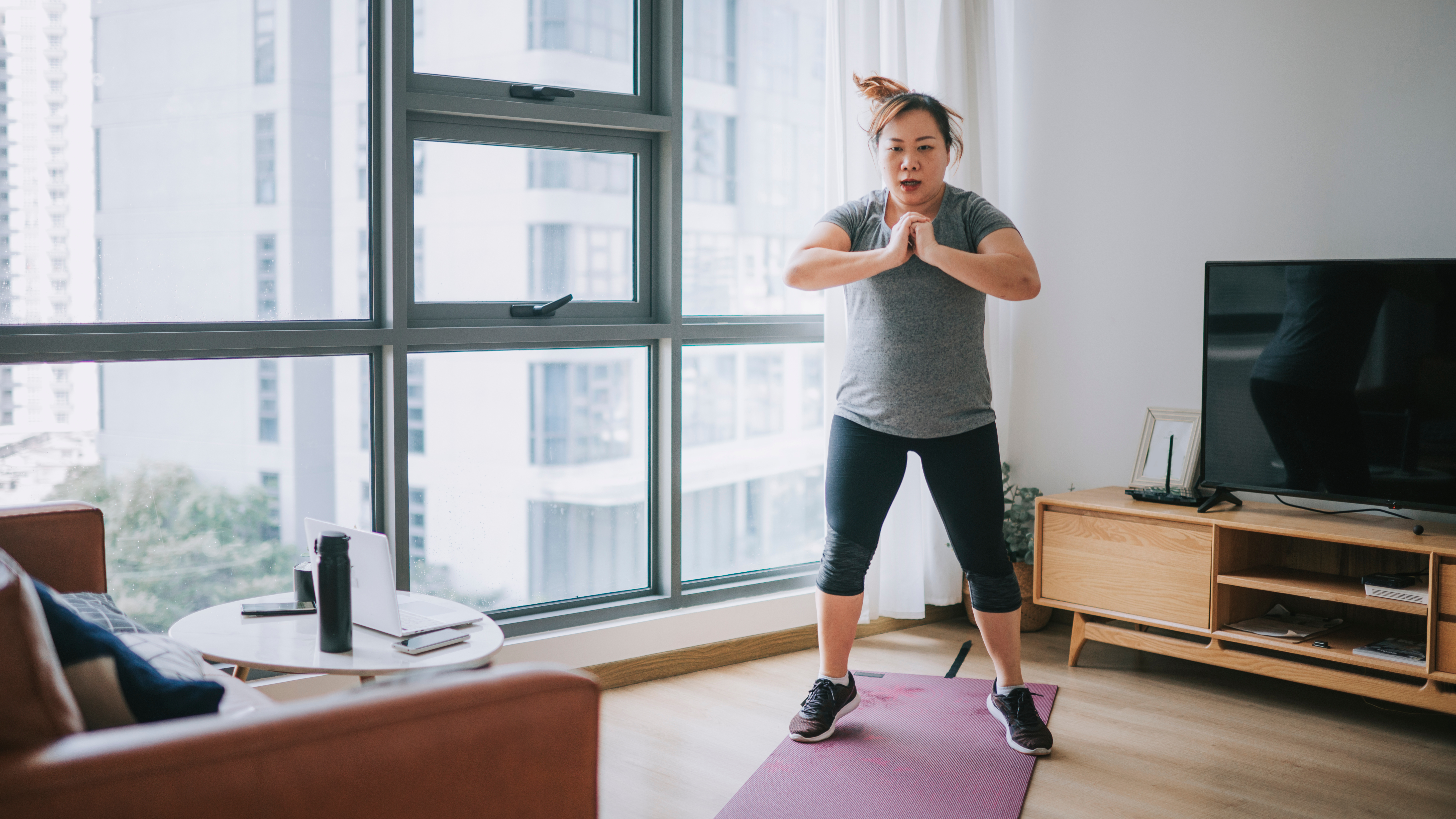 A woman performs jumps in an apartment over an exercise mat.
