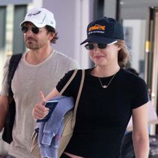 Gigi Hadid wearing a black T-shirt with cropped cargo pants and flip-flops at the airport with Bradley Cooper