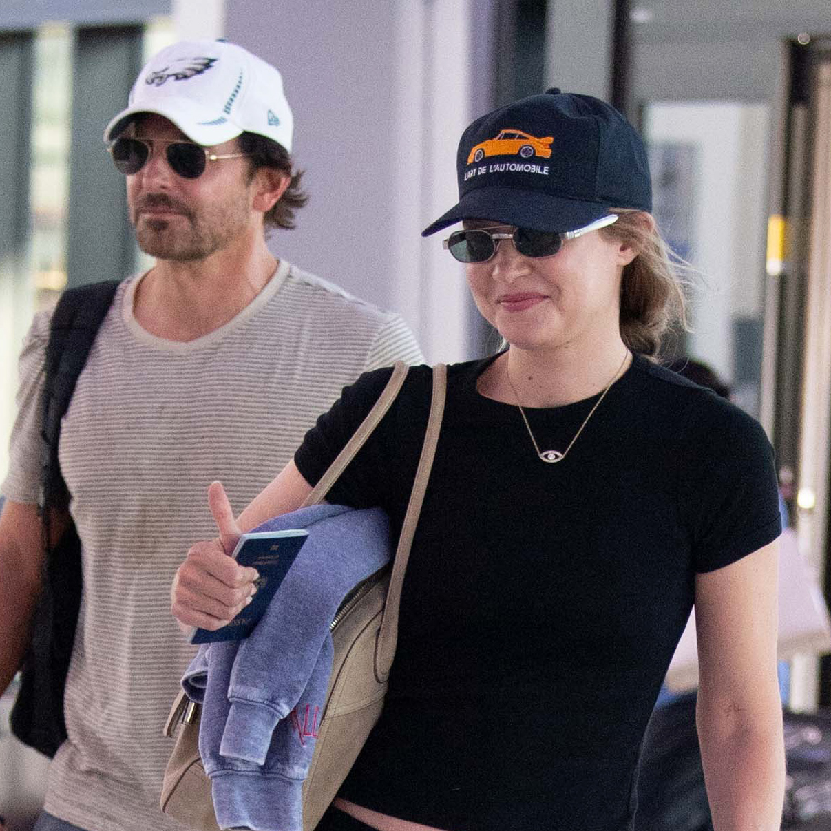 Gigi Hadid wearing a black T-shirt with cropped cargo pants and flip-flops at the airport with Bradley Cooper