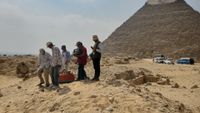 A photograph of a group of archaeologists at a survey site in front of a pyramid.