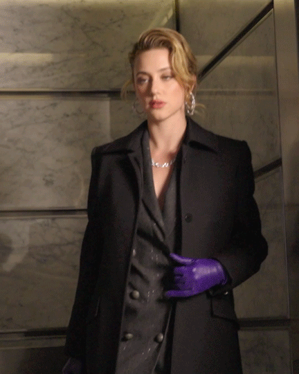 a moving image of Lili Reinhart wearing purple gloves and staring at the camera
