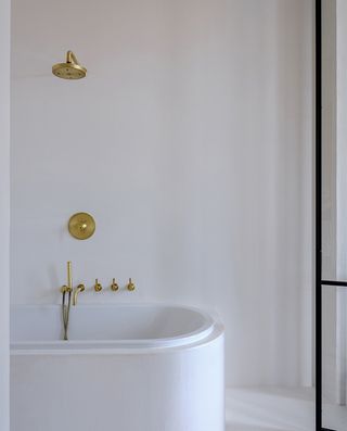 A bathroom with a white tub, bronze taps, bronze shower head and a black clothing rail.