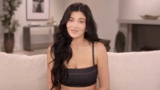 Kylie Jenner in a black crop top staring straight at the camera on the famous confessional couch for The Kardashians.