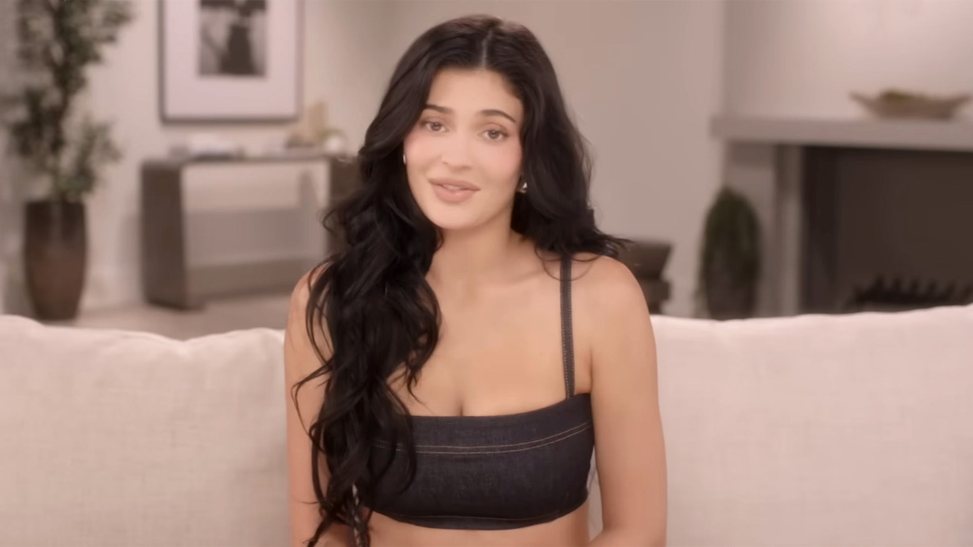 Kylie Jenner in a black crop top staring straight at the camera on the famous confessional couch for The Kardashians.
