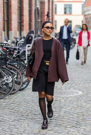 woman wearing burgundy jacket, t-shirt, bermuda shorts, tights, and loafers