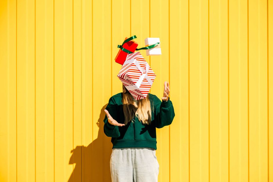A woman is juggling gifts against a yellow wall. 