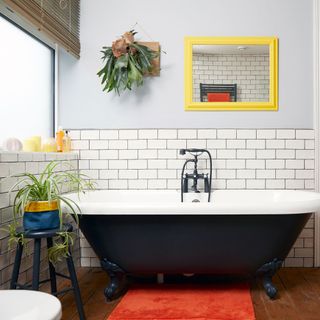 black painted roll top bath with yellow mirror on wall