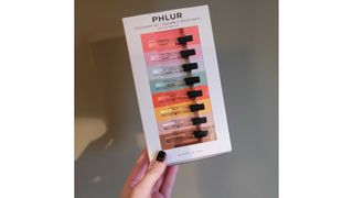 A close up of Digital Beauty Writer, Naomi Jamieson holding the PHLUR perfume discovery set in front of a dark green background