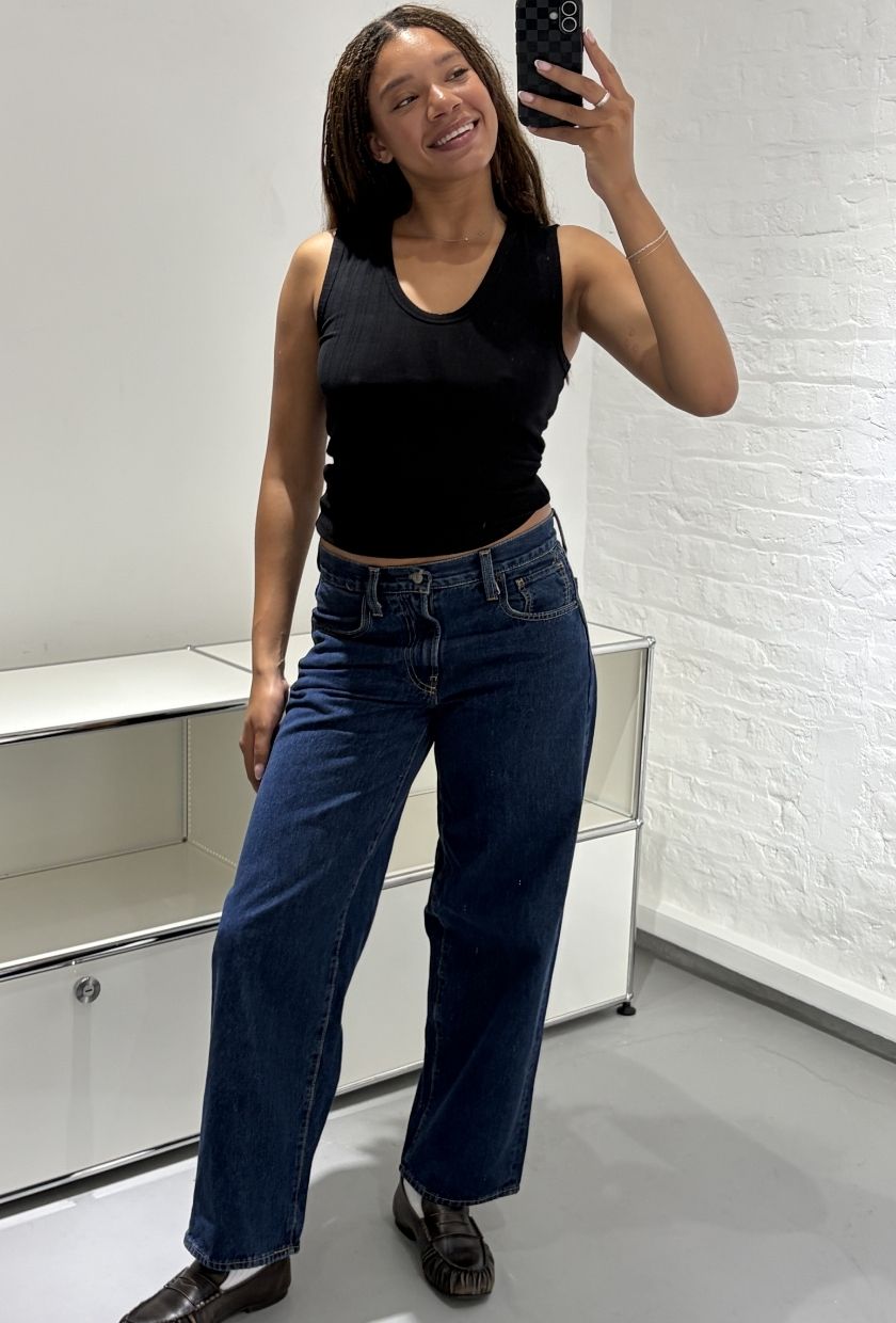 Woman wears black tank top, blue jeans, black loafers