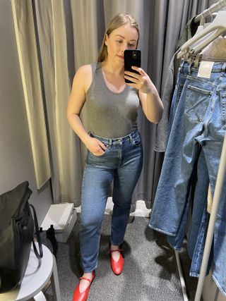 Woman in dressing room wears grey top, blue jeans, red shoes