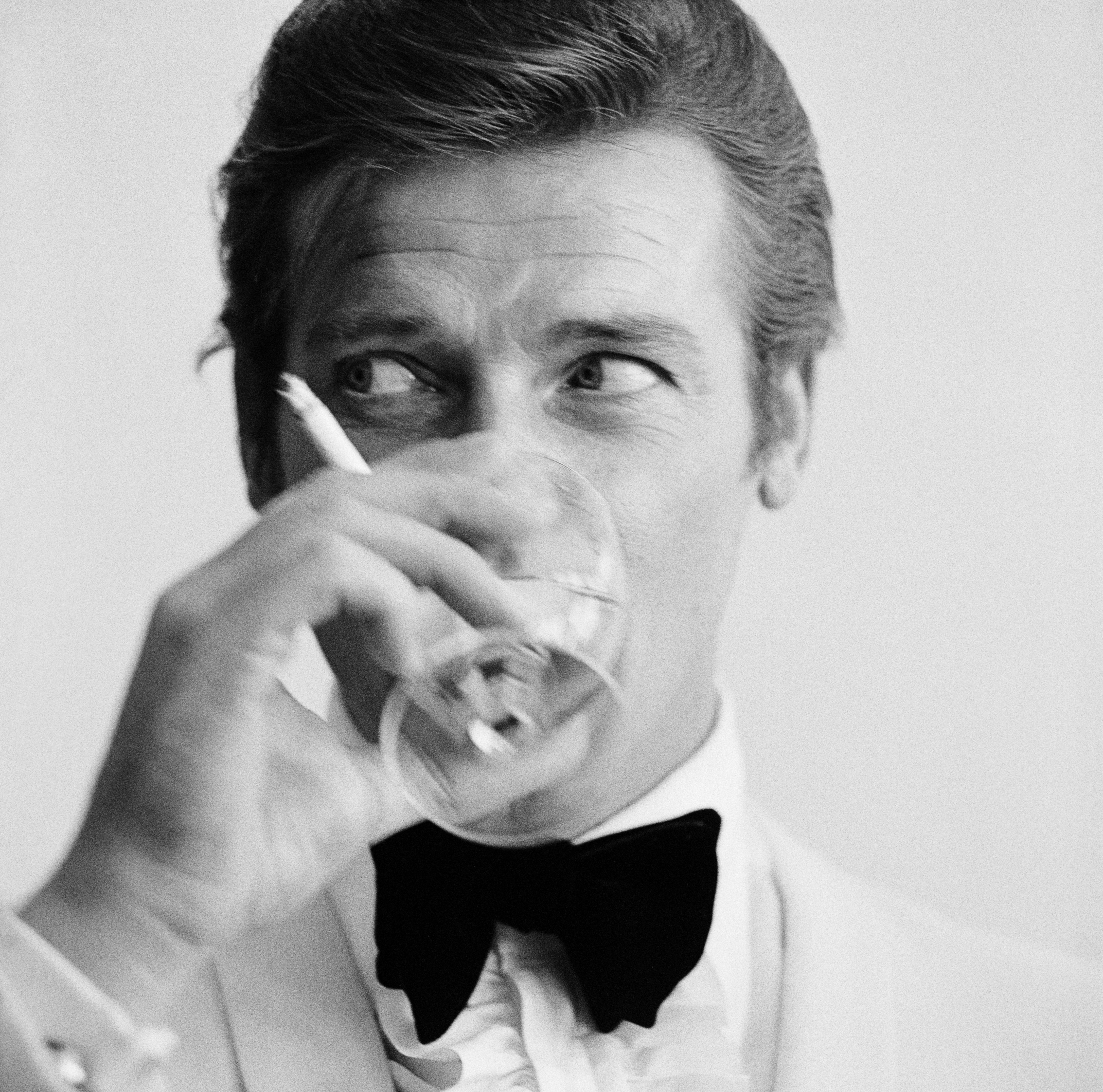 Black and white pictures of Roger Moore in white tie, drinking a martini and smoking a cigarette
