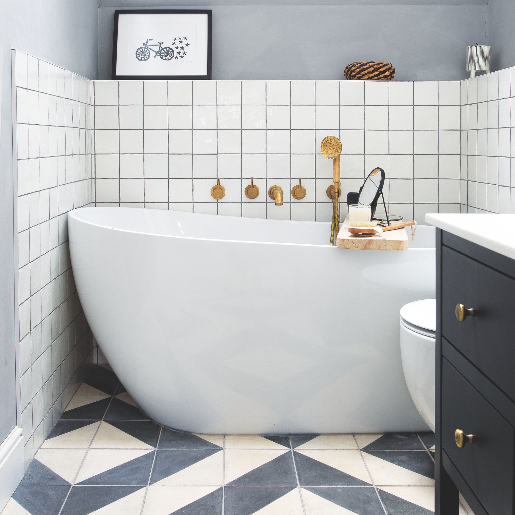 Grey bathroom with white tiles on the wall, and grey and white geometric tiles on the floor, with a freestanding white bath