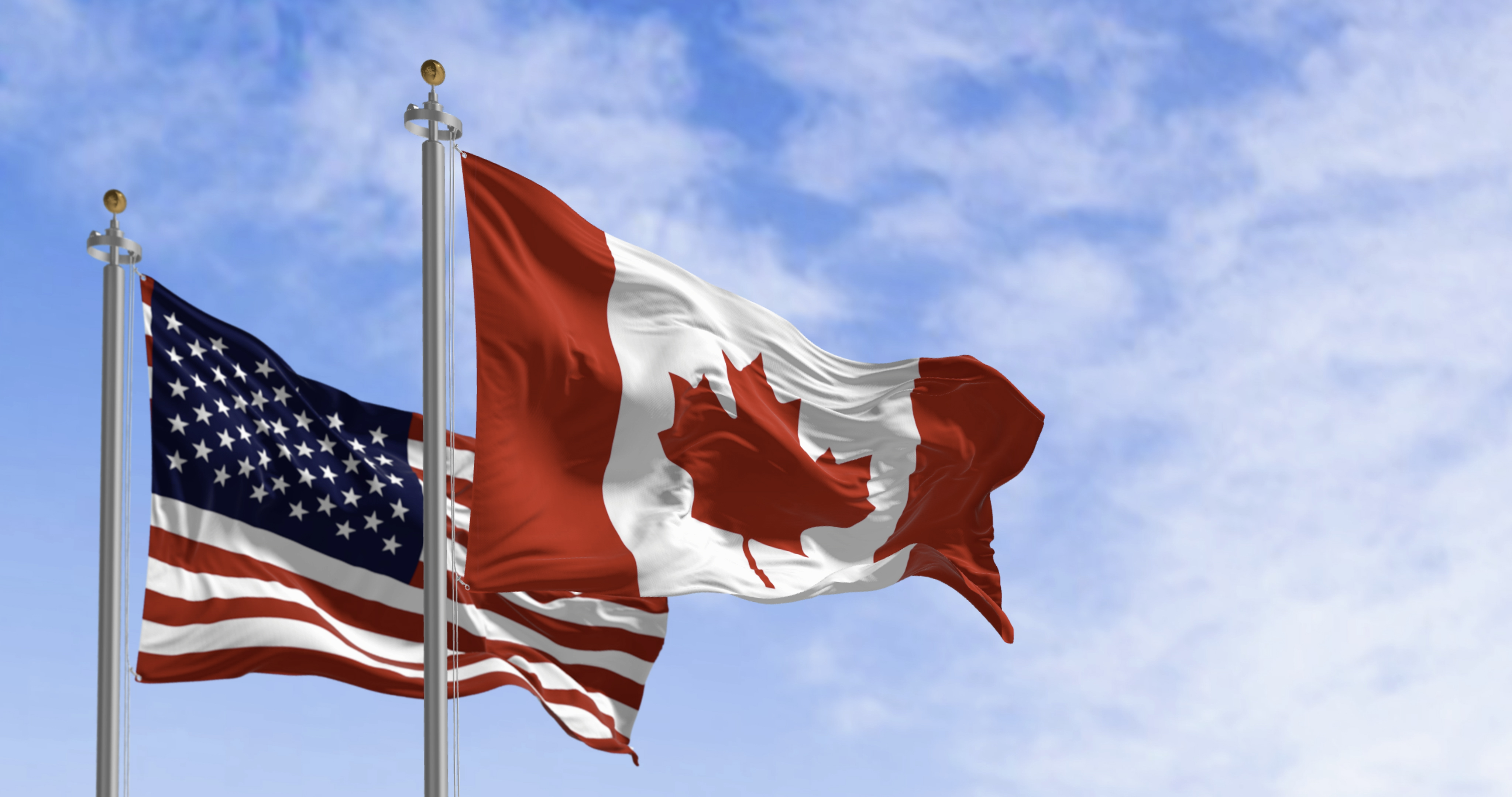 American and Canadian flags waving on a clear day. 