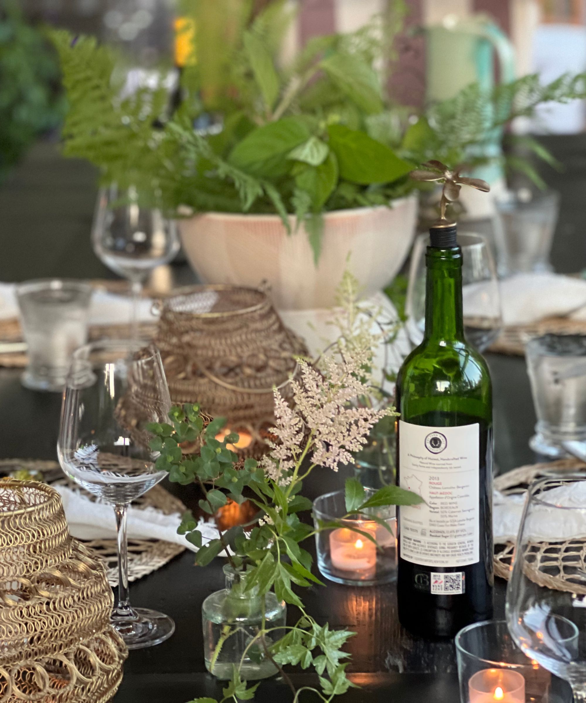 table set with rattan placemats, glassware and greenery in a central bowl and small glass vases