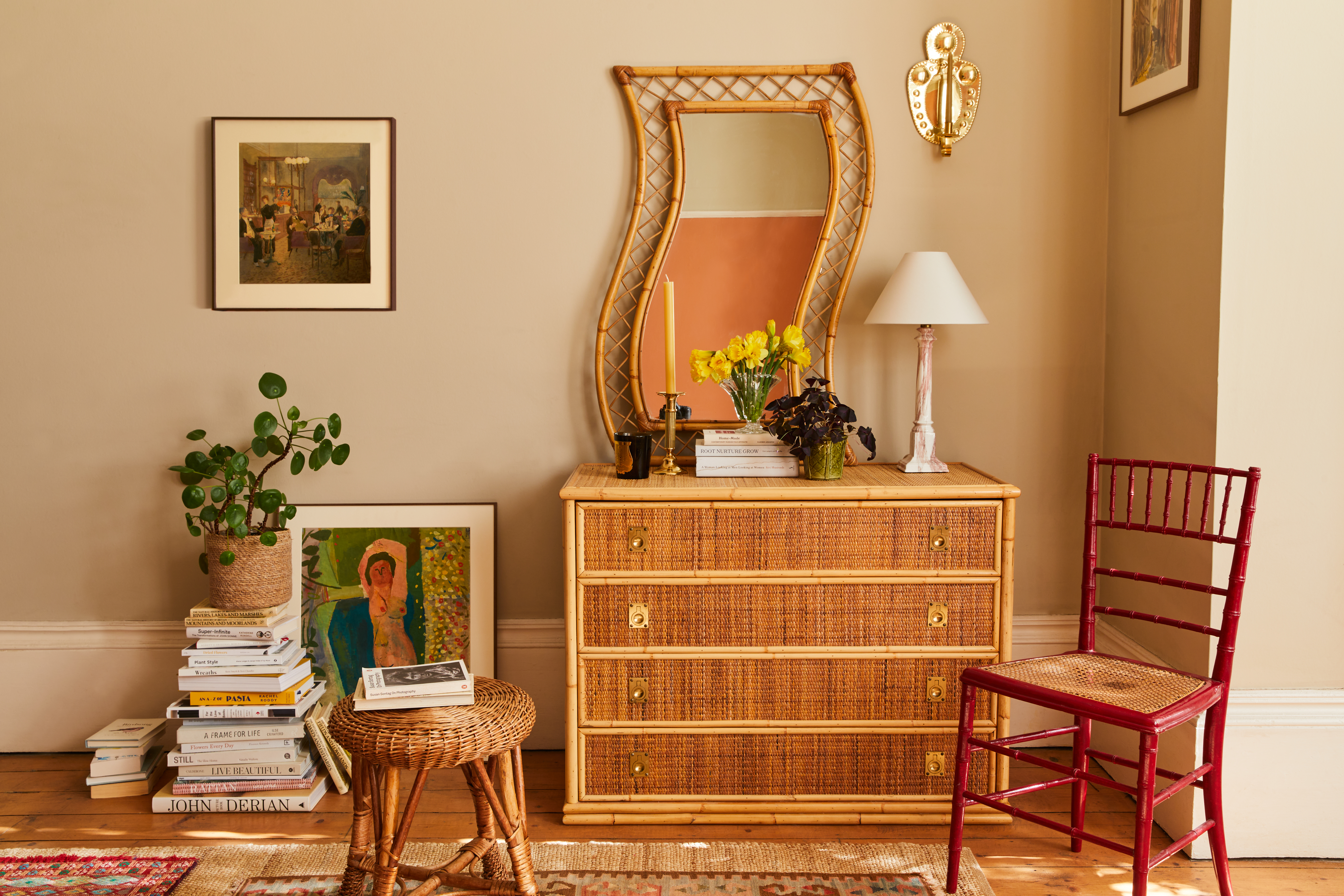 A textured bamboo dresser topped with a unique, wavy-framed rattan mirror, yellow daffodils in a glass vase, and a pink marble lamp against a beige wall.