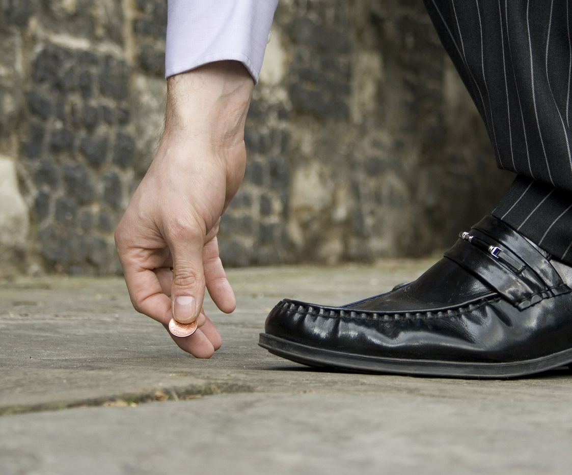 A man picks a coin up from the street.