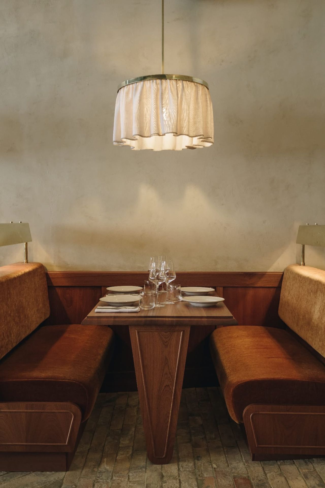 An inventively designed modern bistro features wooden surfaces elevated by sumptuous velvet details, sculptural pendant lighting, and artworks.