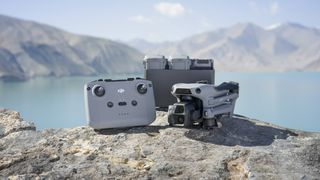 DJI Air 3S drone alongside remote controller and battery charging hub, on a rock with glacial lack and mountain backdrop