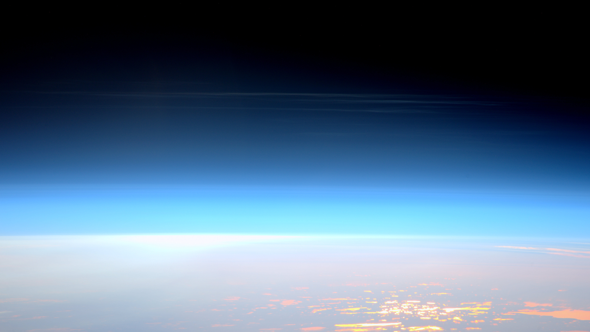 Dunne witte piekerige wolken hoog in de wazige blauwe atmosfeer van de aarde met het aardoppervlak eronder.