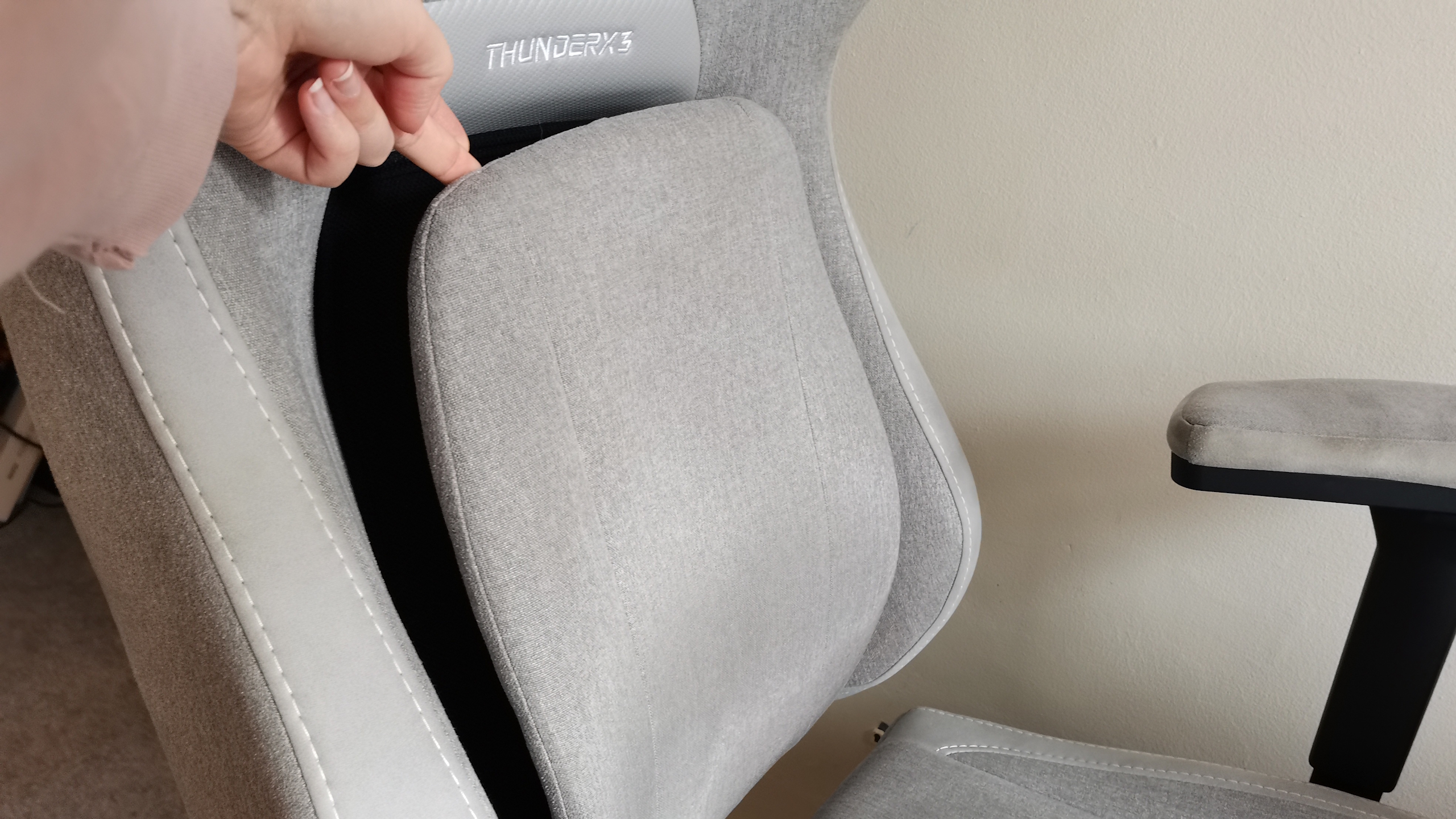 The ThundercoreX3 Core gaming chair in grey in front of a pale wall, next to a wooden bed frame