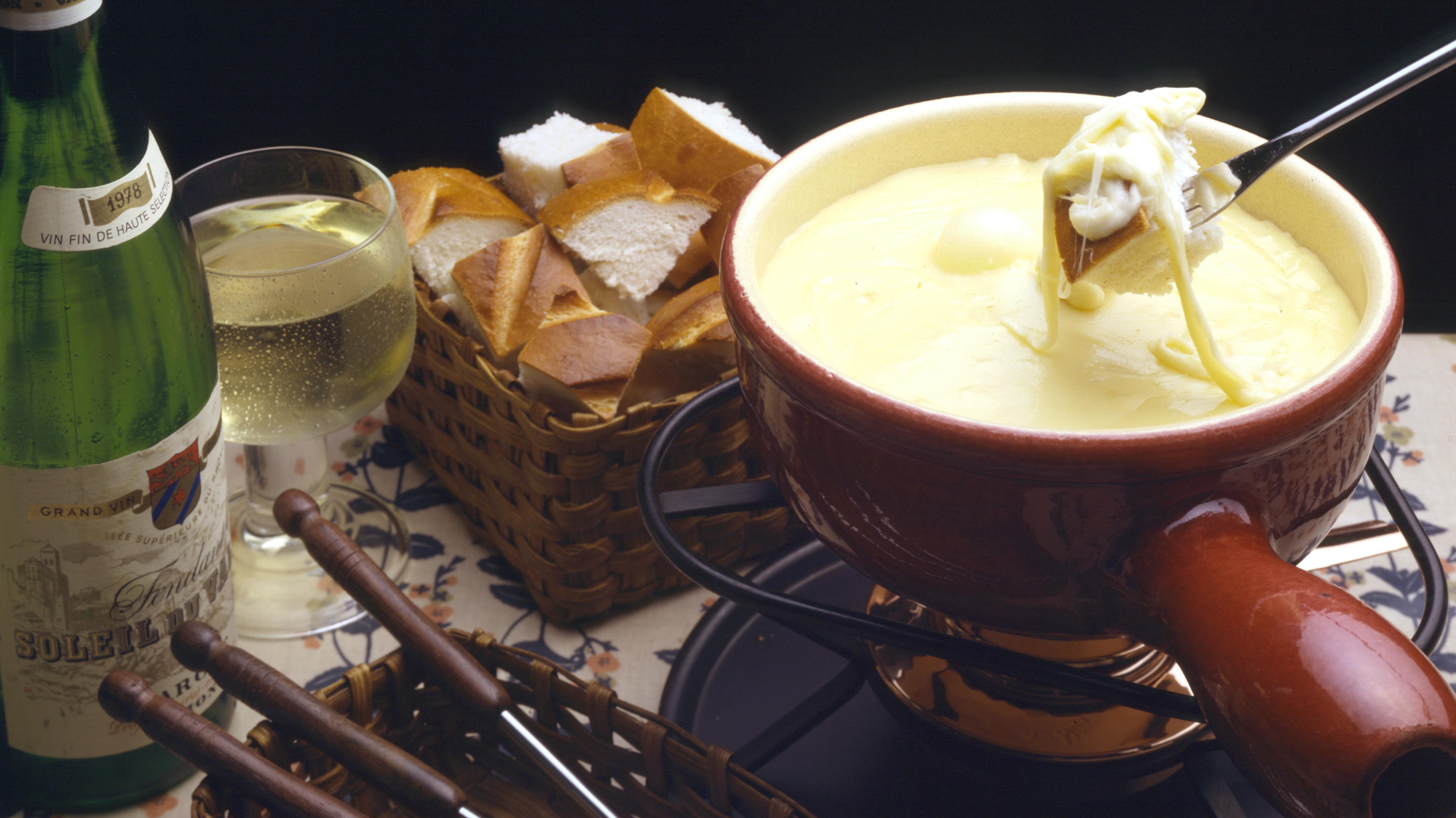 Cheese fondue with a basked of bread and glass of white wine.