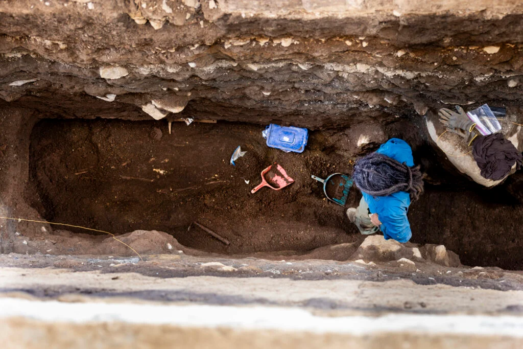 a person in a blue jacket excavates an ancient grave in a deep trench