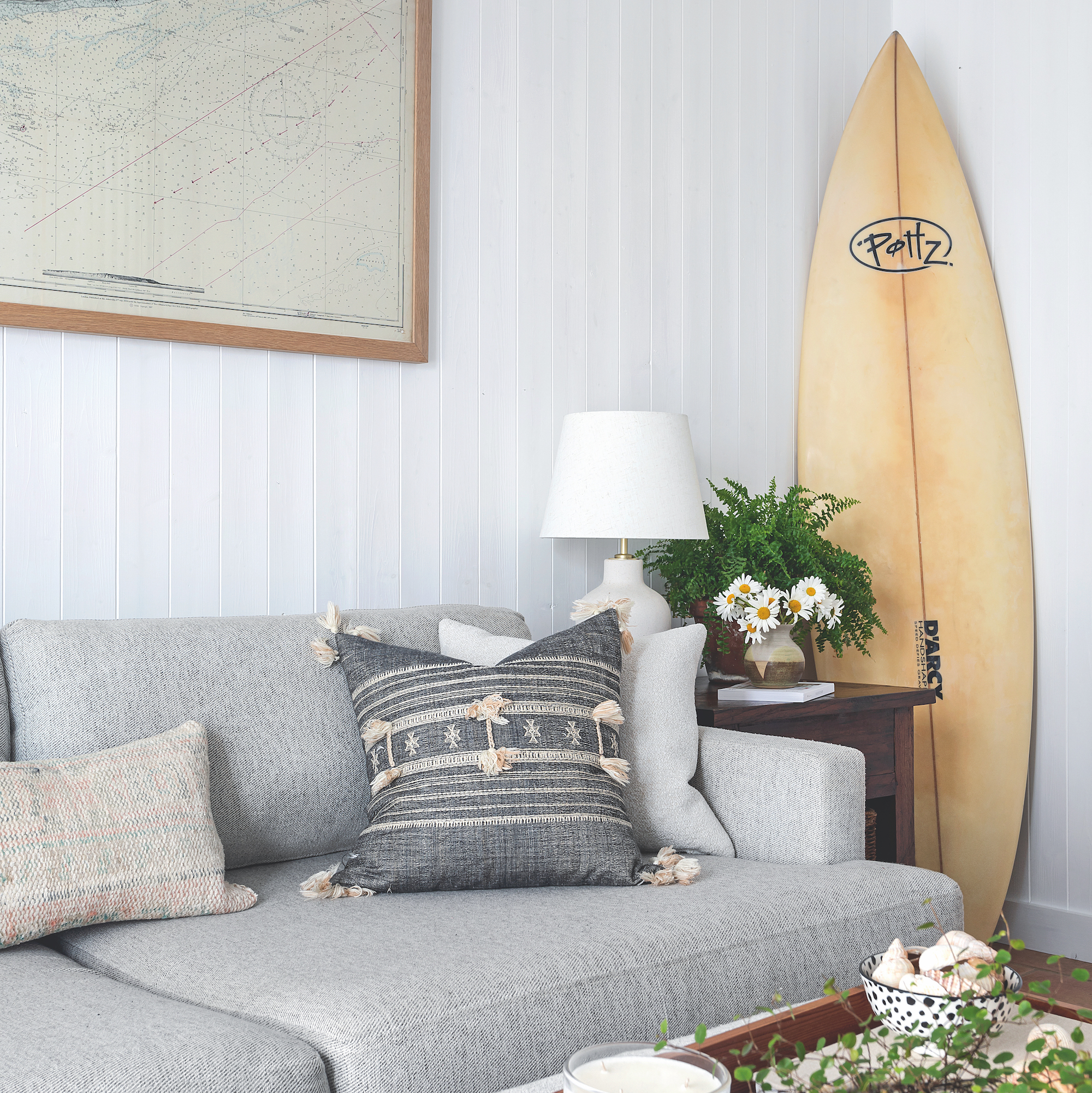 Coastal style sitting room with wood panelled walls and pale grey sofa with surfboard propped against wall