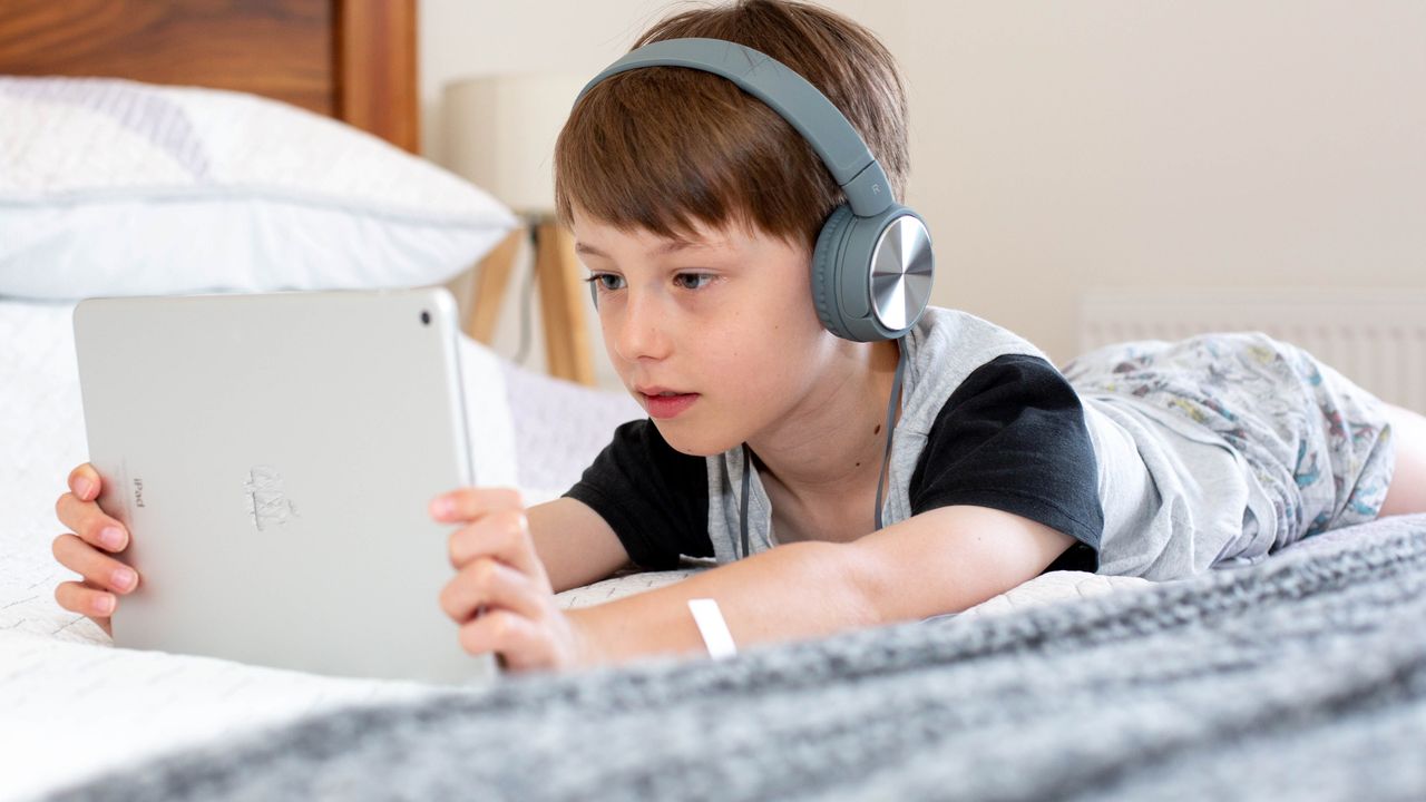 Best tablets for kids: Image depicts boy on bed holding tablet with headphones in