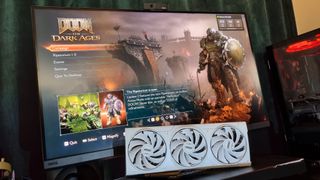 An RTX 5080 GPU sitting in front of a 32-inch 4K screen with Doom: The Dark Ages running on GeForce Now in the background