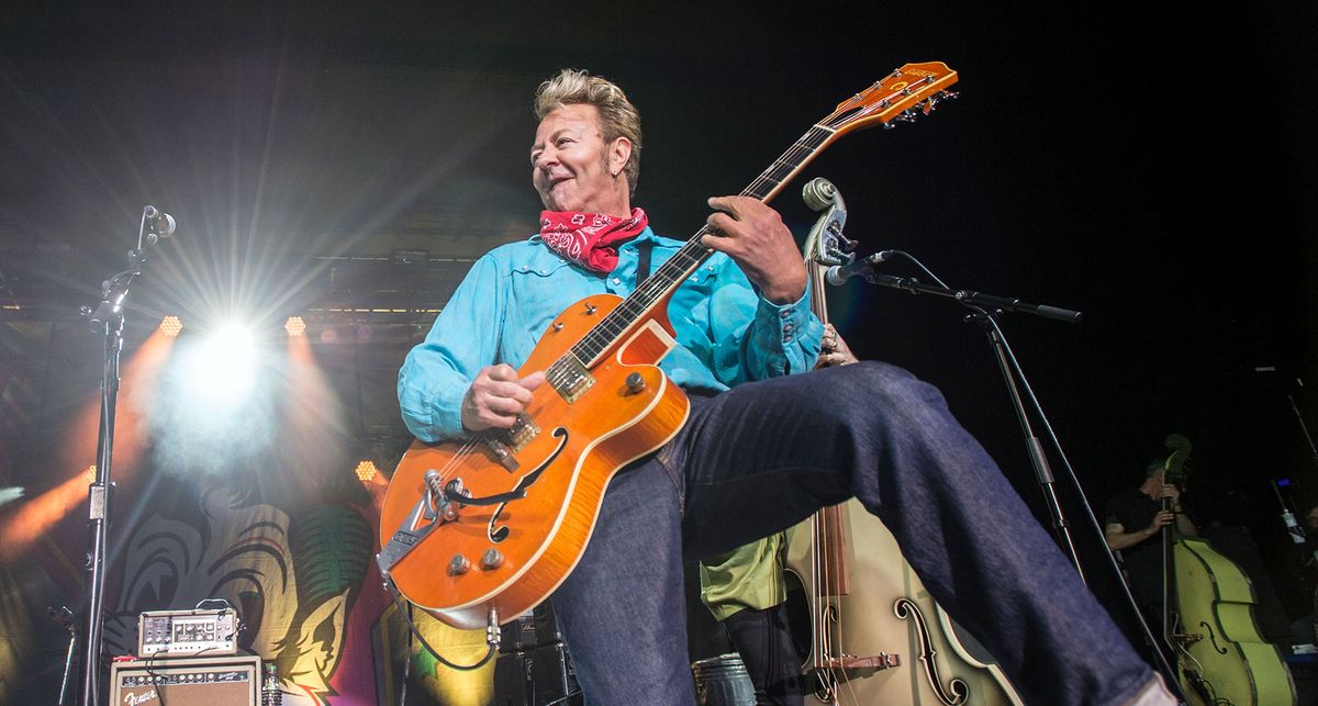 Brian Setzer performs onstage with the Stray Cats: the rockabilly icon wears a bright blue western shirt and red bandana, and plays a Gretsch G6120T in orange.