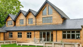 Contemporary timber-clad home with soft green window frames and slate roof, showcasing a stylish blend of natural materials and muted colour tones.