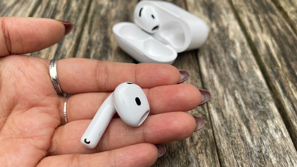 One earbud from the Apple AirPods 4 with ANC in an open hand. In the background, the case is open to show the other earbud inside.