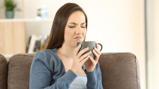 Woman sitting on sofa making a disgusted face while holding a cup of coffee