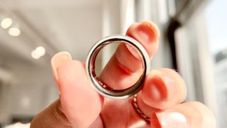 Oura Ring 4 held between a person's fingers