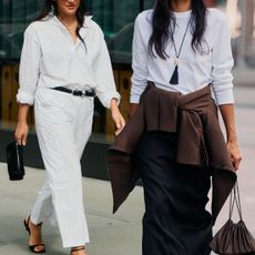 A woman in a white button-down and jeans. A woman in a black skirt and a long-sleeved white shirt with a long pendant necklace. 