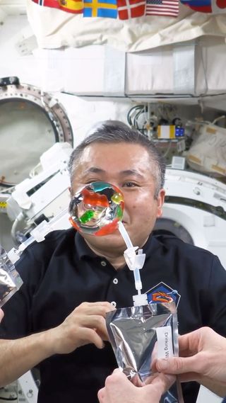 closeup of a male astronaut on the international space station, playing with a sphere of water with gummi bears embedded in it