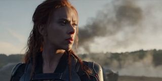 Natasha Romanov stands in front of billowing smoke in a scene from Black Widow