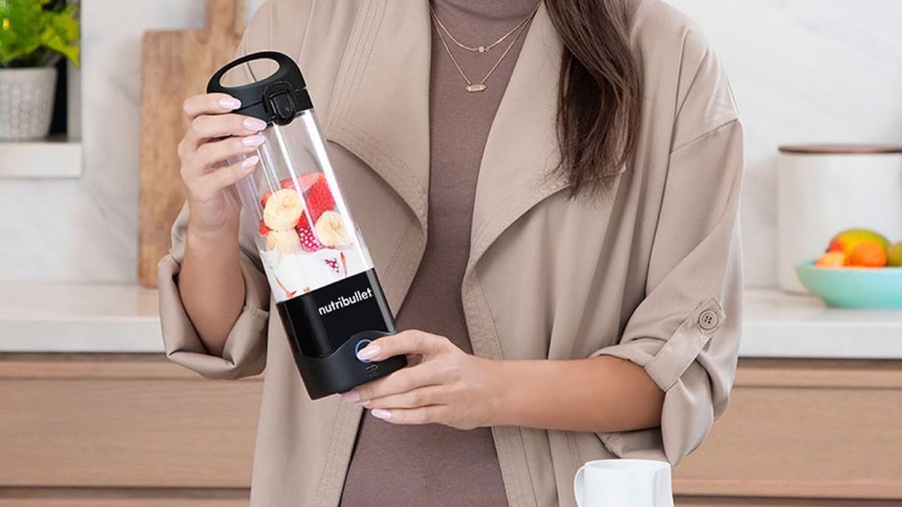 A woman holding the Nutribullet Portable Blender whilst it makes a strawberry smoothie