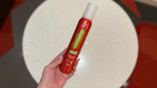 A red Wella Shockwaves Volume mousse can held upright in a hand against a neutral background, with branding and “Volume” label