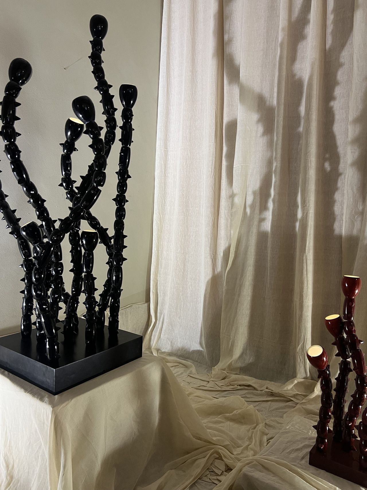 Image of a large, sculptural black lamp that resembles a gothic-inspired coral plant. It's sitting on a platform covered in draped fabric.