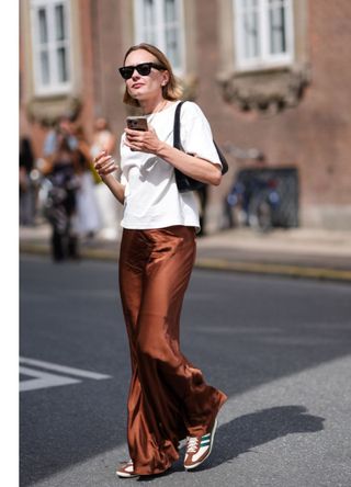 A woman wearing a boxy tshirt with a long ochre silk skirt