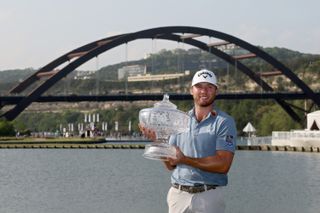 Sam Burns holds a trophy in front of the Austin bridge