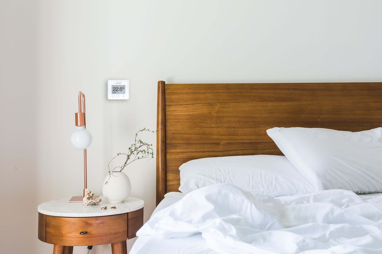 WundaSmart thermostat on a bedroom wall above as bedside table