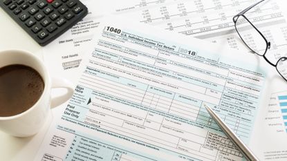Income tax return form with espresso cup, calculator, glasses and pen on table